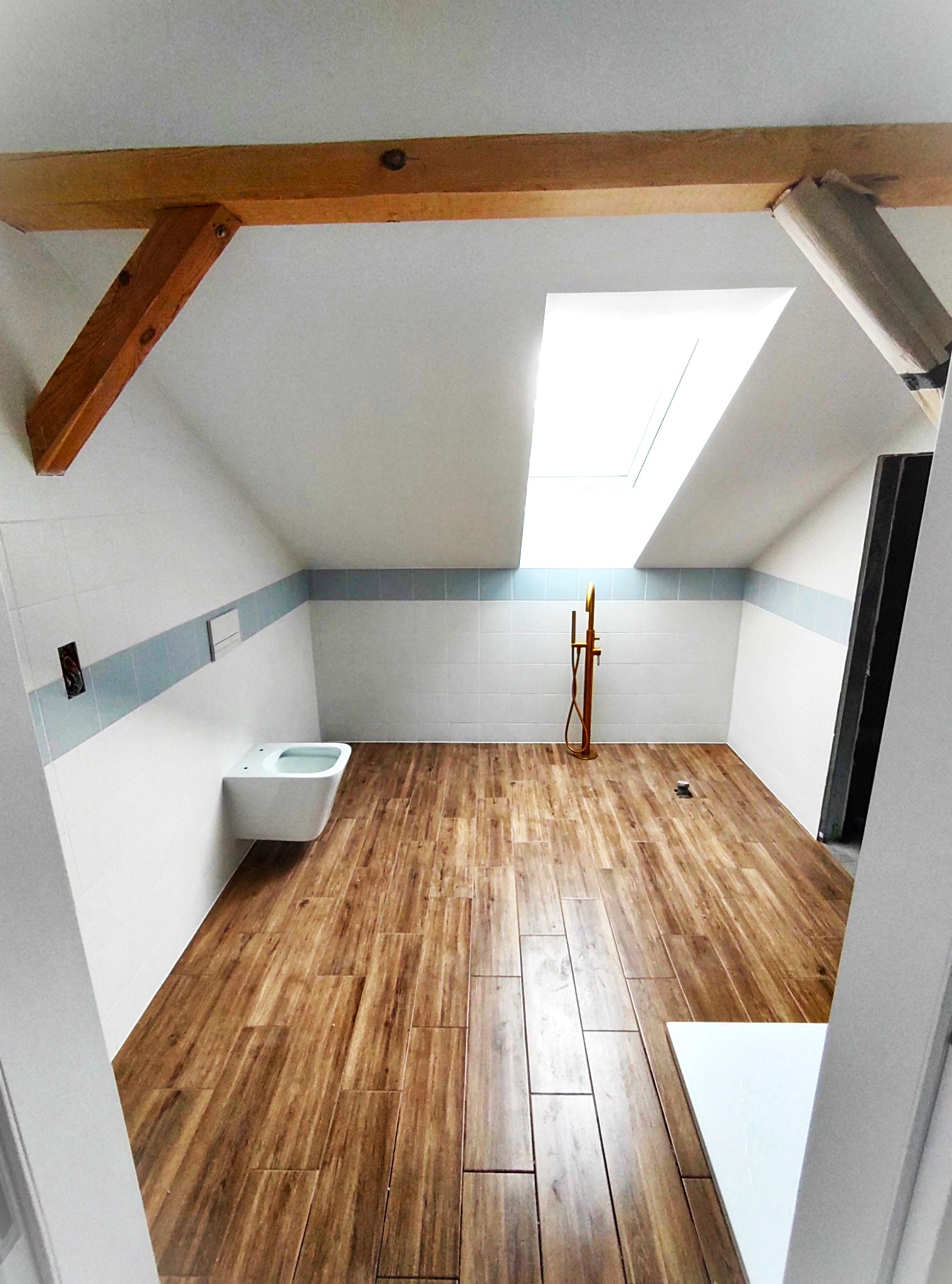 biała łazienka z oknem dachowym i terakotą o wzorze drewna